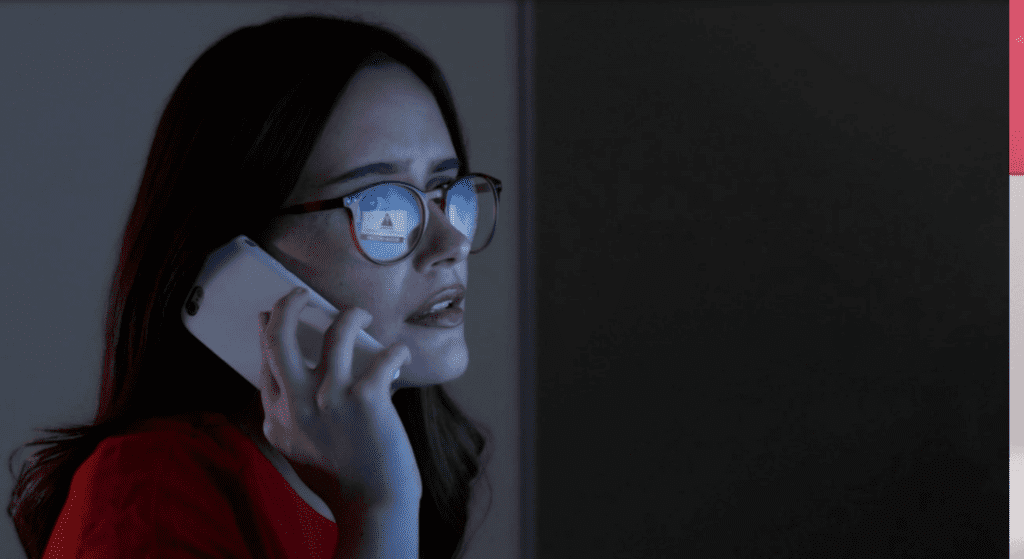 Person on phone looking at fraud notification on computer