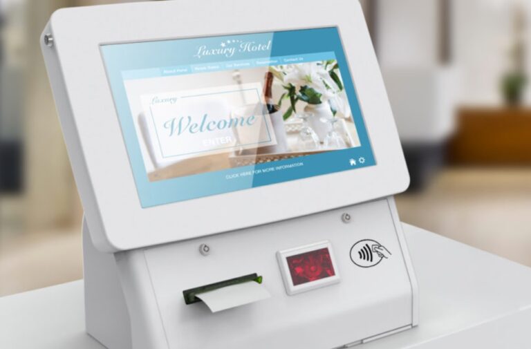 A white computer screen on a table-top kiosk by ImageHolders, displaying a hotel welcome screen and a contactless card payment system